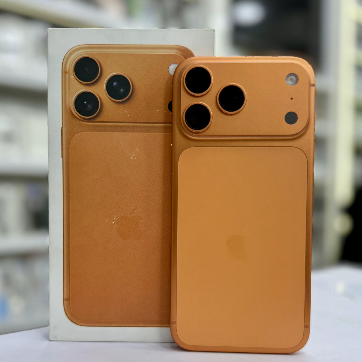 An orange phone back skin or decal applied to a smartphone, shown in front of its white retail box. The skin covers the camera cutouts and back panel, with the Apple logo visible through a slight cutout.
