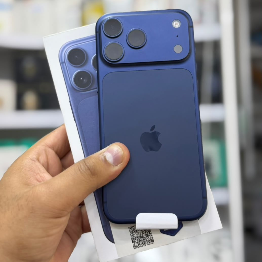A hand holds a blue Apple iPhone showing the back of the phone and its retail box in a store setting.